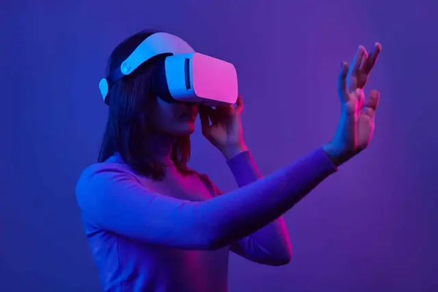 Young woman wearing a white virtual reality headset with one hand outstretched, under violet and pink light suggesting a digital environment
