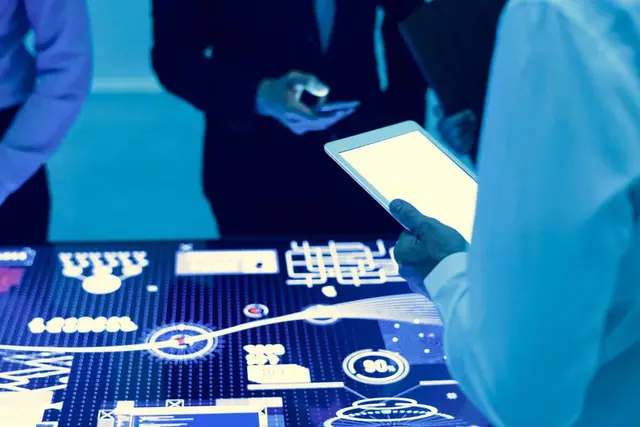 People holding a tablet and a phone in front of a glowing table with charts and indicators in blue tones