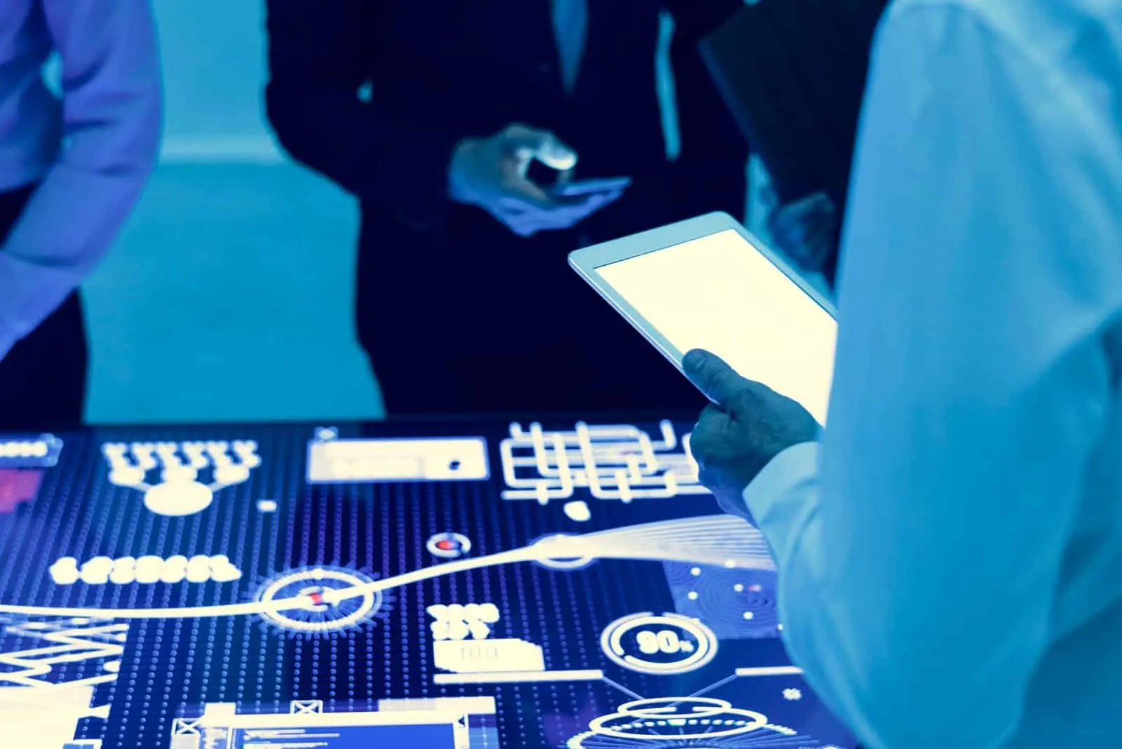 People holding a tablet and a phone in front of a glowing table with charts and indicators in blue tones