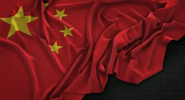 Flag of China with one large yellow star and four smaller ones, crumpled against a dark background
