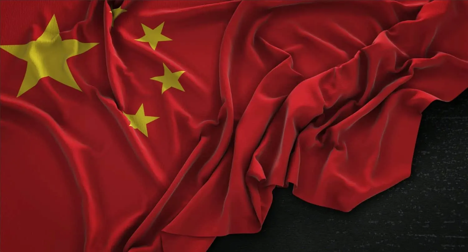 Flag of China with one large yellow star and four smaller ones, crumpled against a dark background