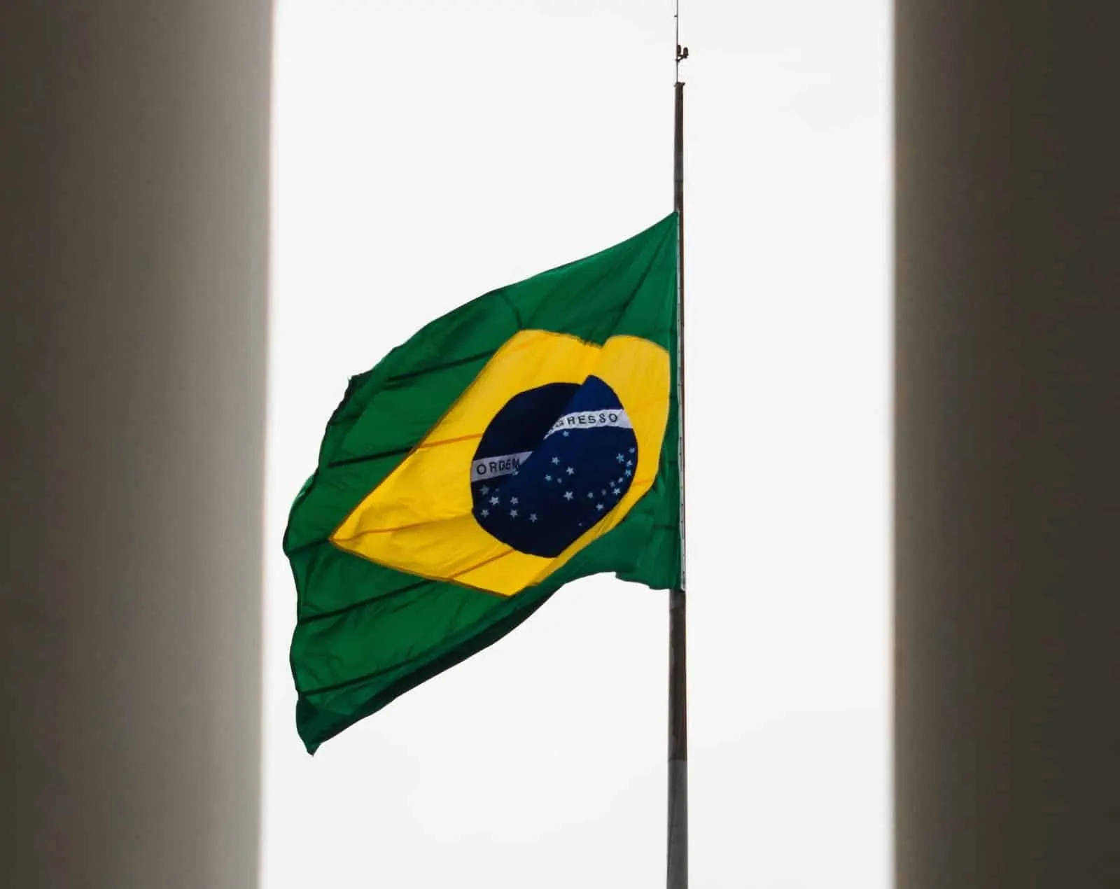 Brazilian flag flying at half-mast against a white sky, framed by two dark walls