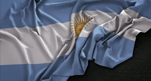 Argentine flag in light blue and white with the golden sun, crumpled and resting on a dark background.