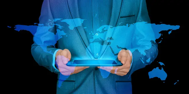 Man in a suit holding a tablet from which a blue hologram of a world map rises