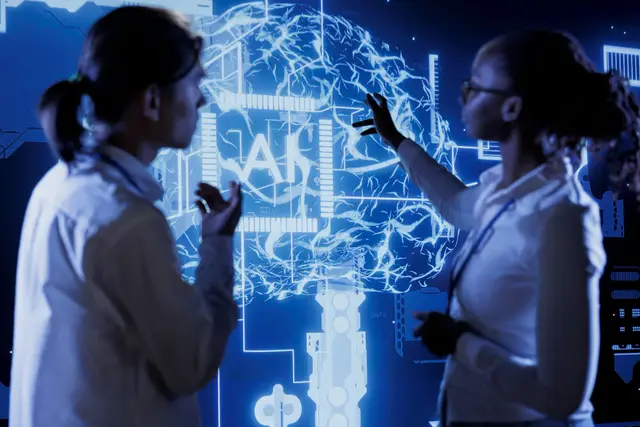 Two people in white coats in front of a large screen showing a glowing brain and a chip with the letters AI, in a blue setting.