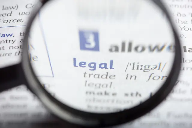 Magnifying glass enlarging the word “legal” in a dictionary entry, with blurred blue and gray lettering around it.