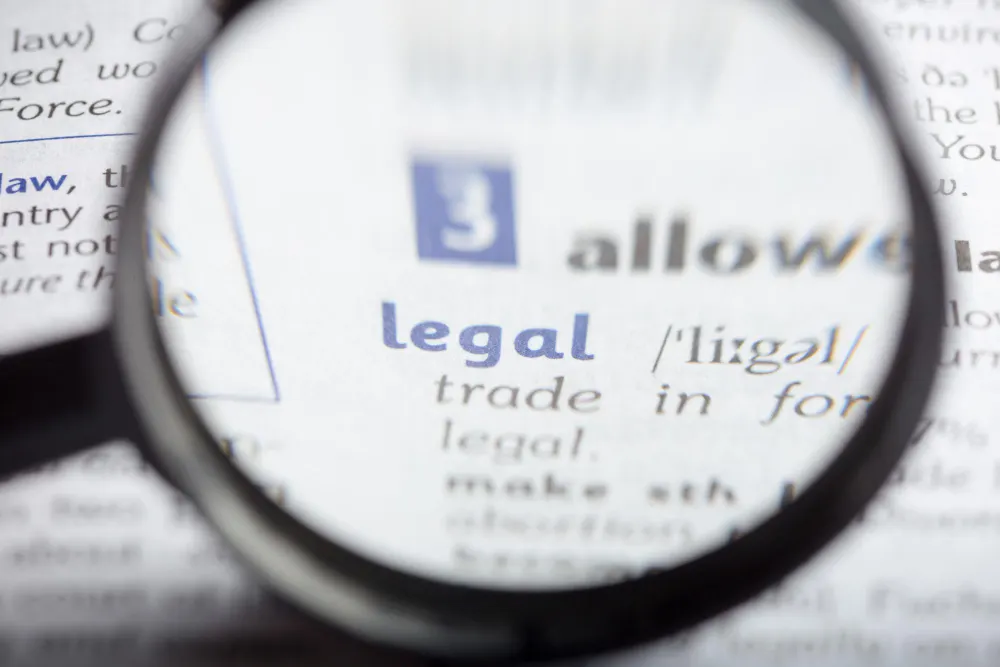 Magnifying glass enlarging the word “legal” in a dictionary entry, with blurred blue and gray lettering around it.