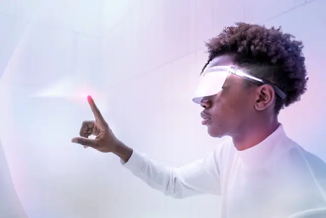 Young person wearing a transparent visor points a finger at a pink point of light against a white and violet background.