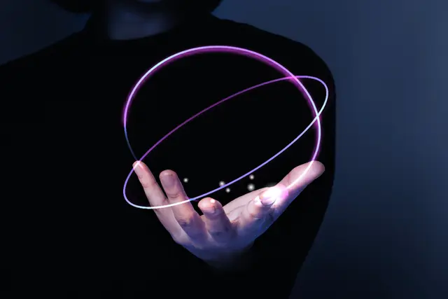 An open hand of a person dressed in black holds a glowing violet double ring that forms a sphere.
