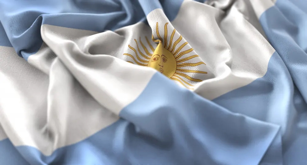 Close-up of a rumpled Argentine flag with light blue and white stripes and the Sun of May at the center.