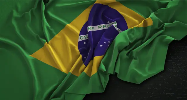 Rumpled Brazilian flag with the yellow rhombus and blue circle with stars, against a dark background.