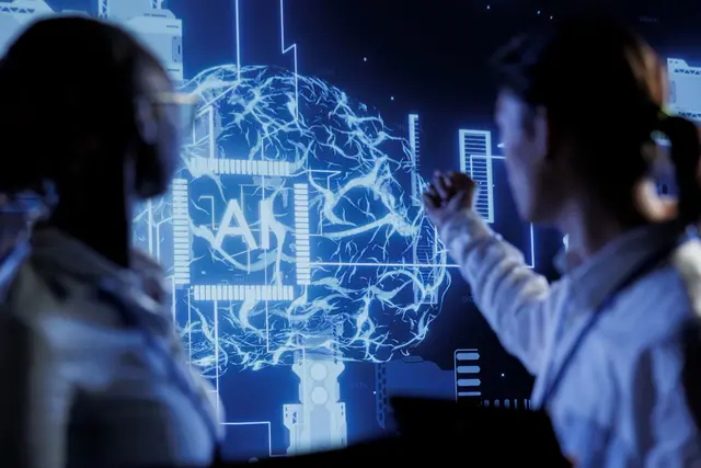 Two people in front of a blue screen showing a brain made of glowing lines with the letters AI at its center.