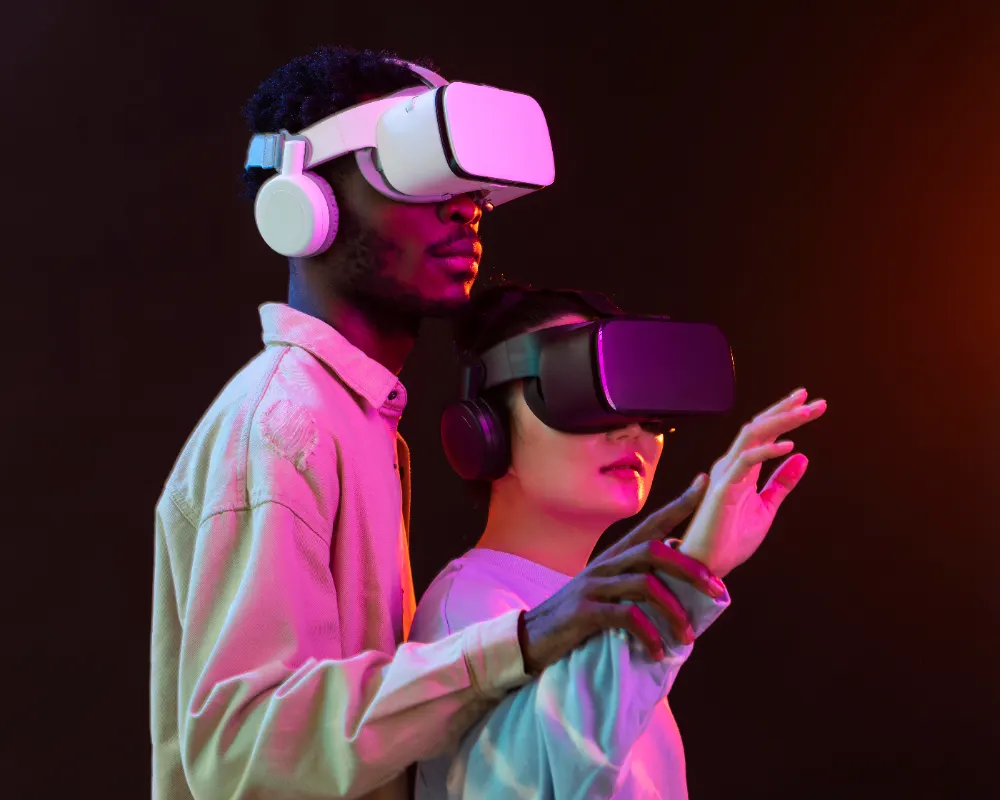 Two people in virtual reality headsets and earphones under pink and blue light; one raises a hand as if touching something ahead.