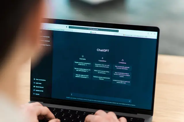 Person typing on a laptop showing the ChatGPT home screen with examples, capabilities and limitations of the chatbot