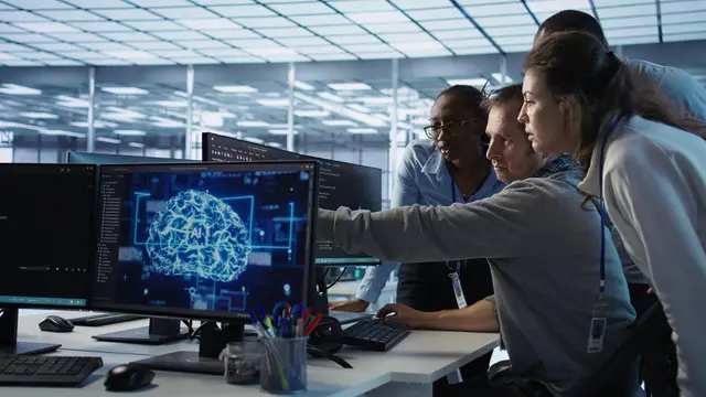 A team of professionals looks at a monitor showing a digital brain with the letters AI in a bright office