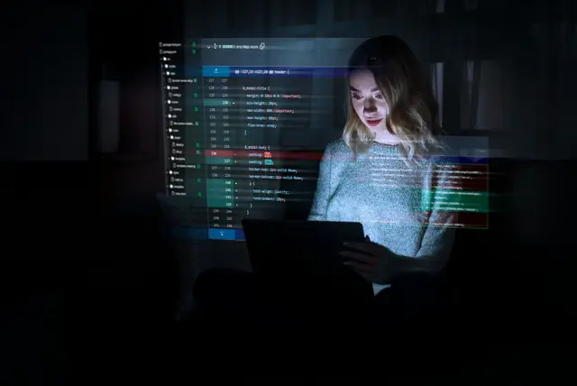 Woman at a laptop in a dark room with lines of code projected over her, an image of artificial intelligence software development