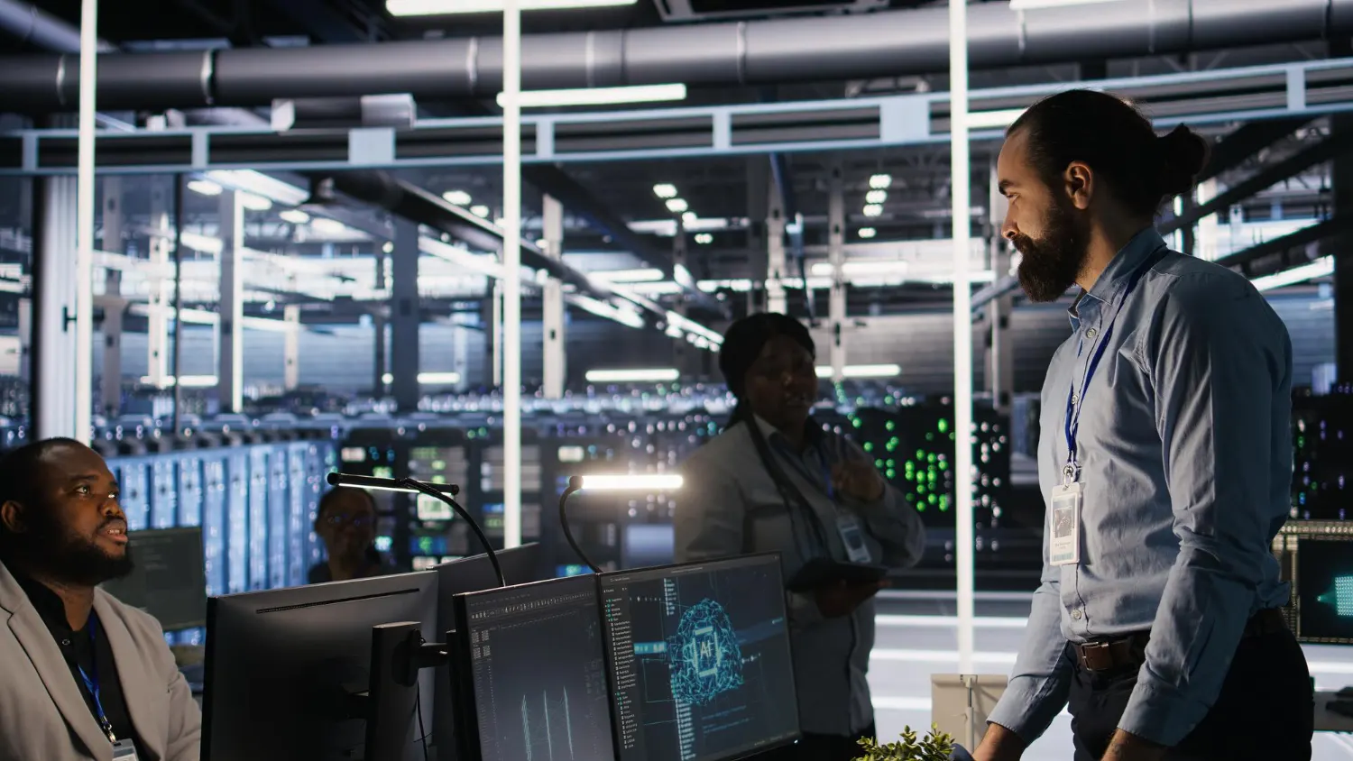 A man talks with colleagues in front of monitors in a bright server room
