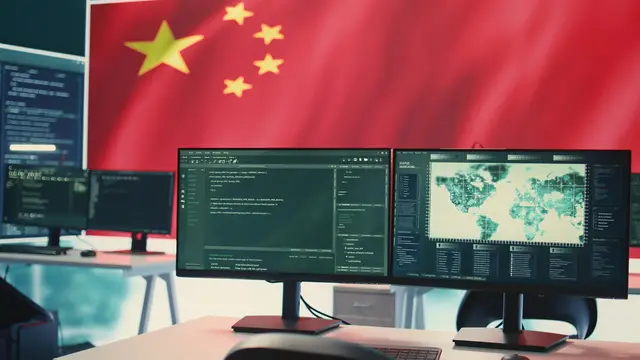 Chinese flag behind two monitors showing code and a map on a work desk