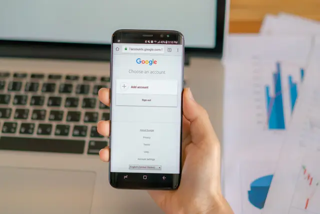 Hand holding a phone with the Google sign-in screen, next to a laptop and printed charts