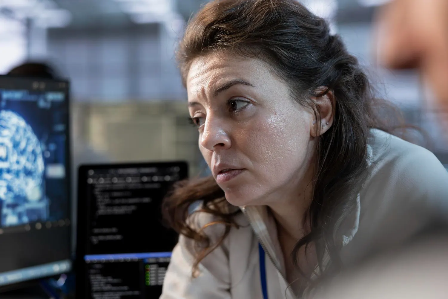 Focused woman in front of monitors showing a digital brain and lines of code in a control room