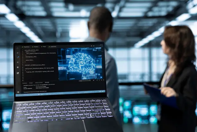 Laptop showing a digital brain on screen with two professionals talking in the background