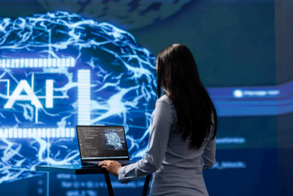 Woman in front of a screen showing a digital brain and the letters AI, with a laptop on a stand