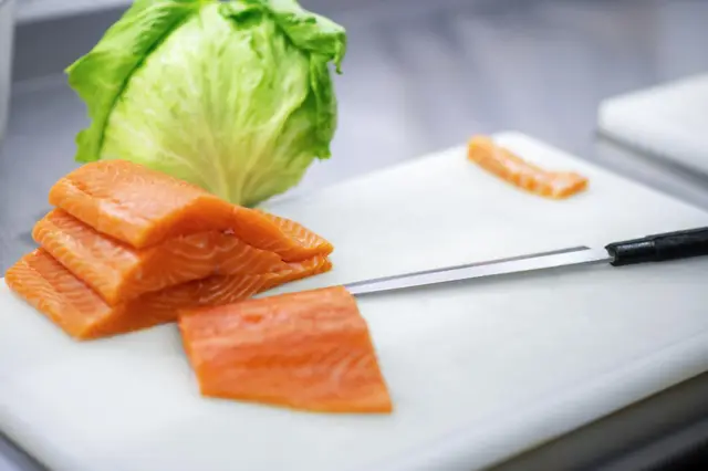 Raw salmon fillets on a white cutting board next to a lettuce leaf