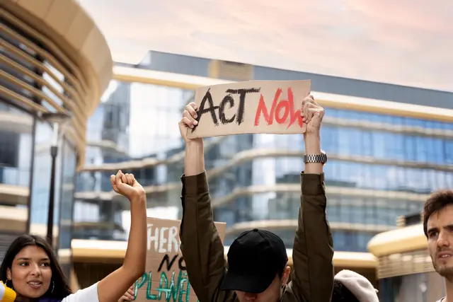 Protesters holding an «Act Now» sign in front of modern office buildings