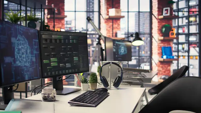 Workstation with several monitors showing a digital brain and code, in a bright office with brick walls