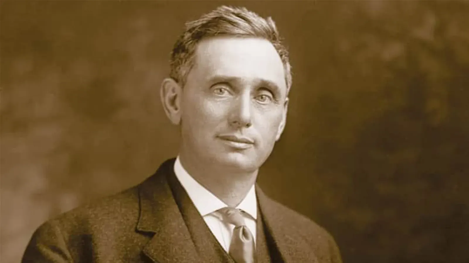 Sepia portrait of a short-haired man in a dark suit, white shirt and tie, an image of Judge Louis Brandeis