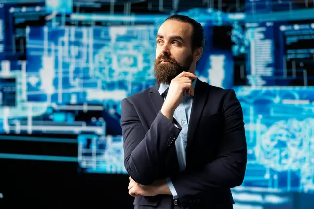 Bearded man in a suit with his hand on his chin, thinking, against a blue background of glowing circuit and brain diagrams