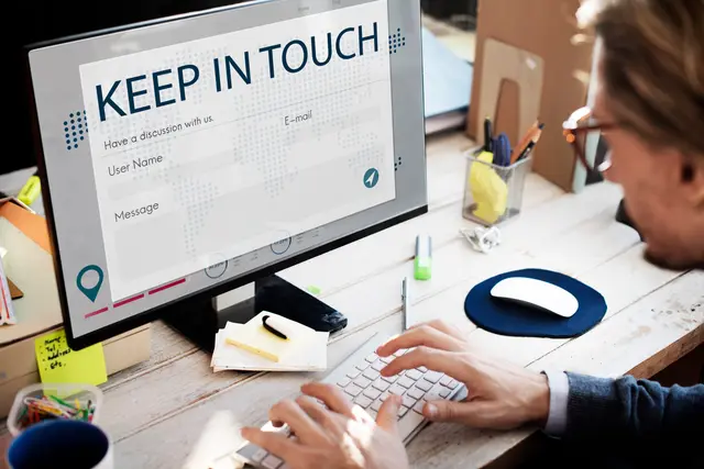 A man with glasses typing on a keyboard in front of a monitor showing a contact form titled “Keep in touch”