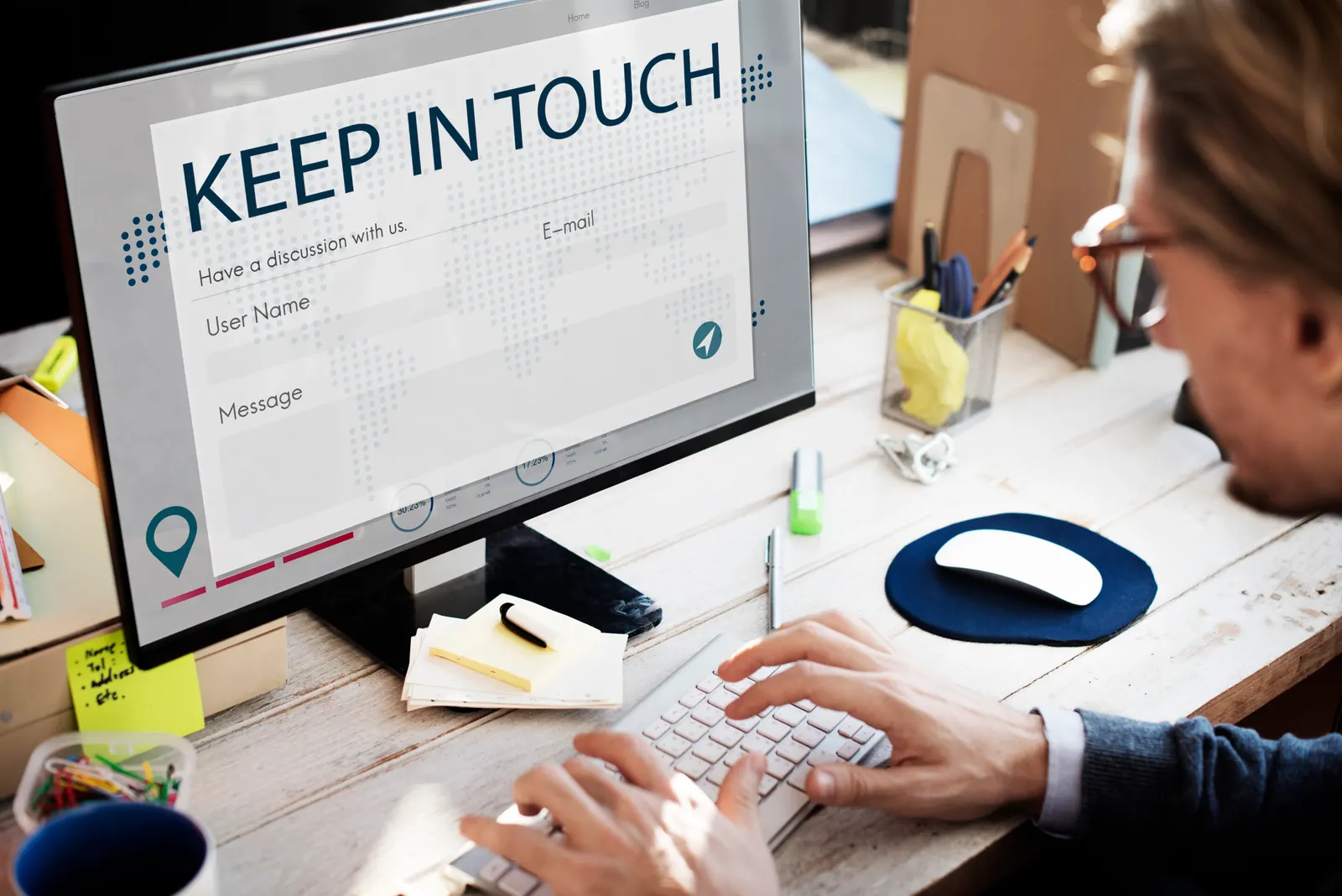 A man with glasses typing on a keyboard in front of a monitor showing a contact form titled “Keep in touch”