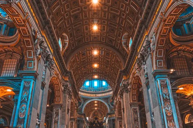 Interior of a basilica with a coffered vault, arches, and ornate columns under warm light